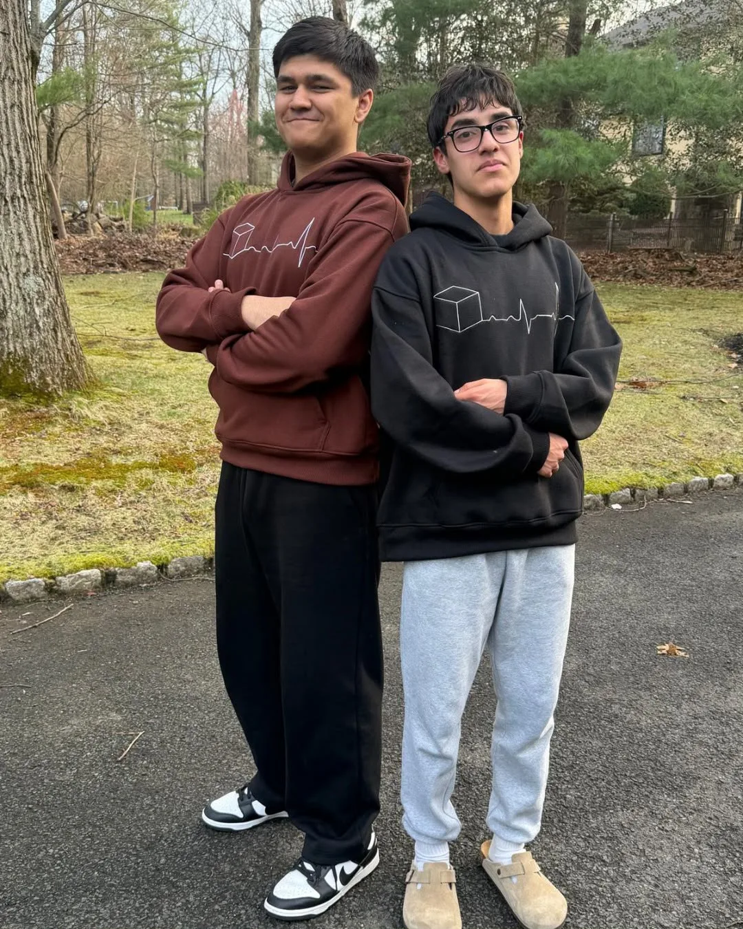 Two models in brown and black hoodies together; brown is campaign styling only